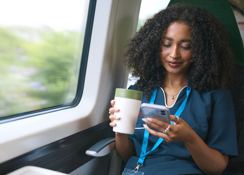 Photo of nurse on her phone while riding a bus and drinking a coffee