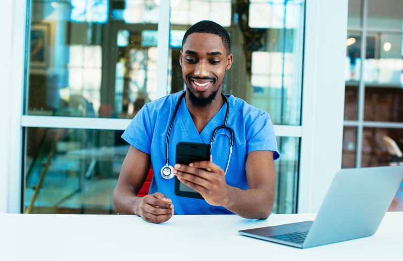 Photo of black male nurse sitting with laptop and phone